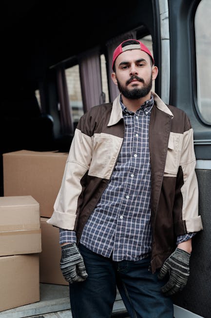 Two movers from Man with Van West Kensington are engaged in a home relocation process, carefully loading a large, dark green piece of furniture into the open rear of a black van parked on a street. Th